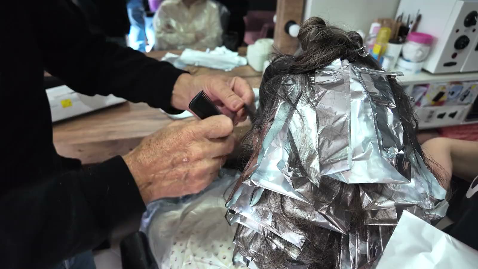 Hands folding foils into hair for color