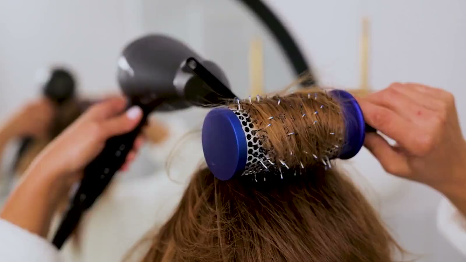 A round brush and a dryer shaping a lock of hair
